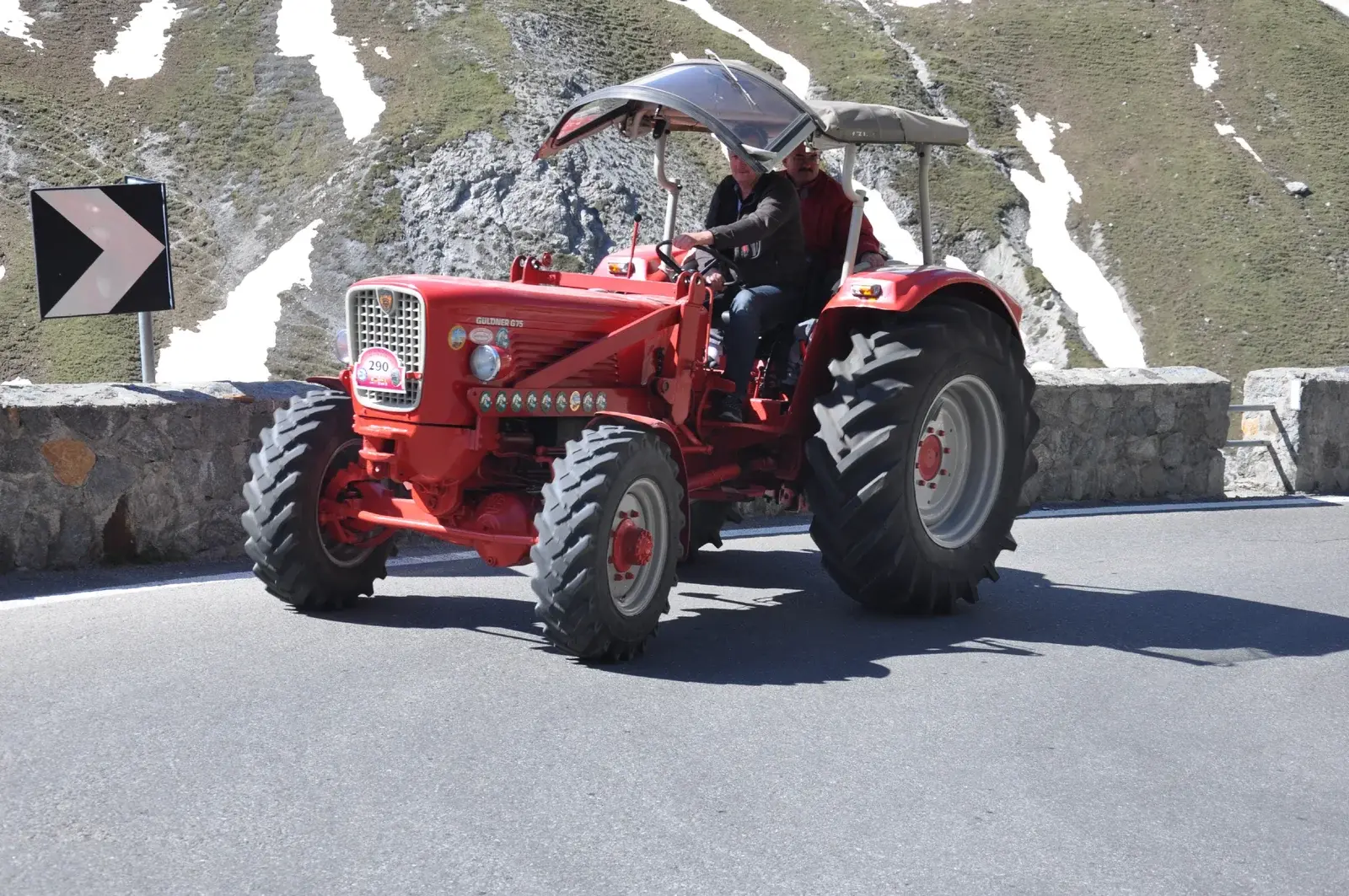 Roter Oldtimer-Traktor mit Vereinsmitgliedern auf der Passstrasse am Stilfserjoch